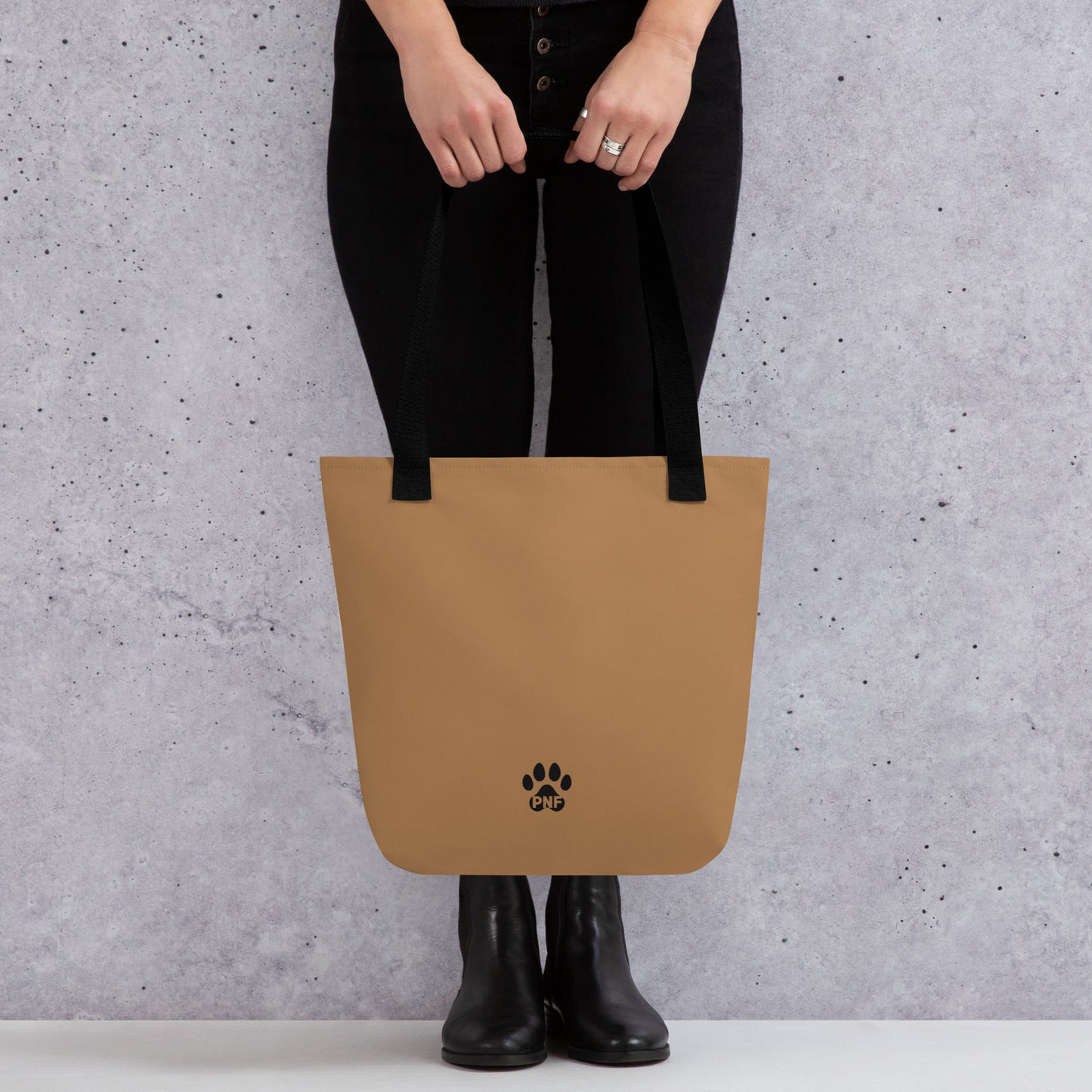 Person holding a tan tote bag with a paw print logo against a gray background