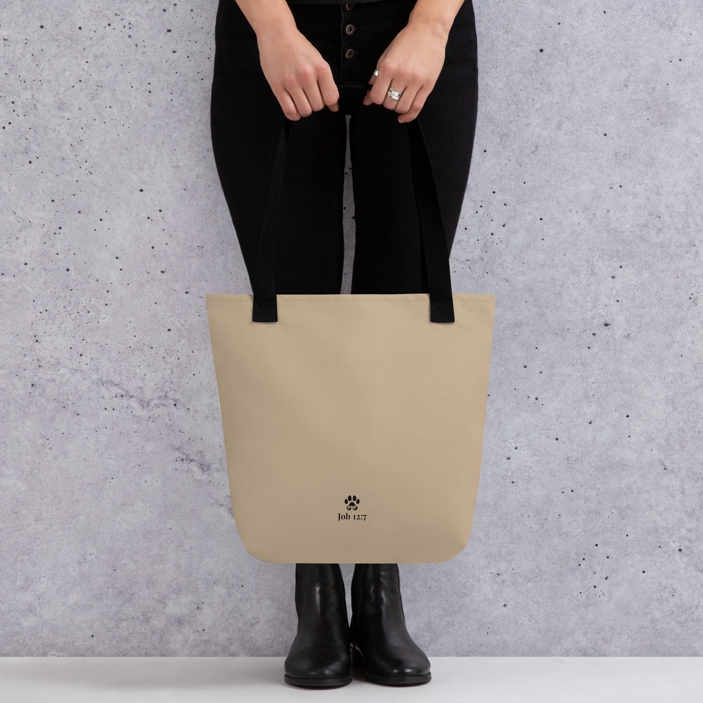 Person holding a beige tote bag with a brand logo against a gray background