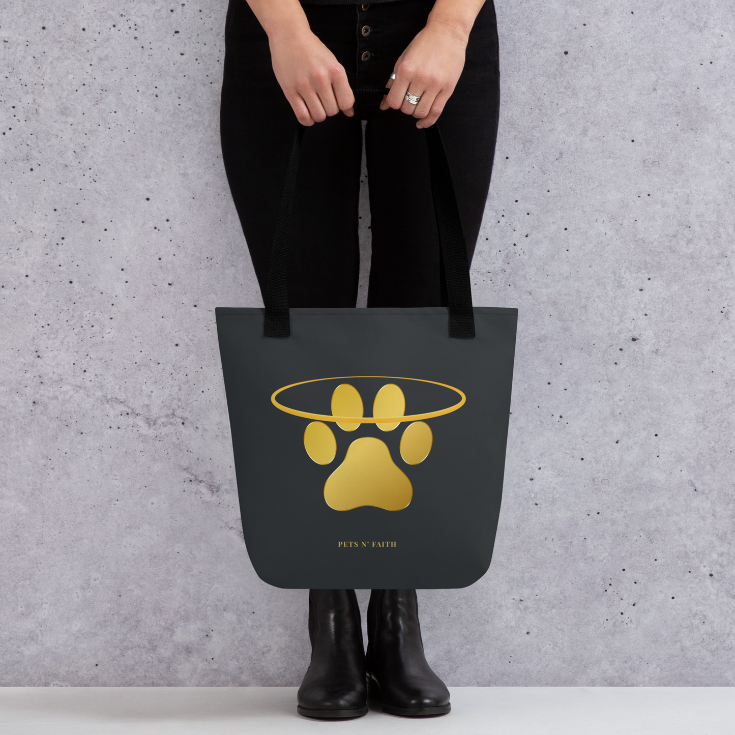 Person holding a dark grey tote bag with a gold paw print design against a gray background