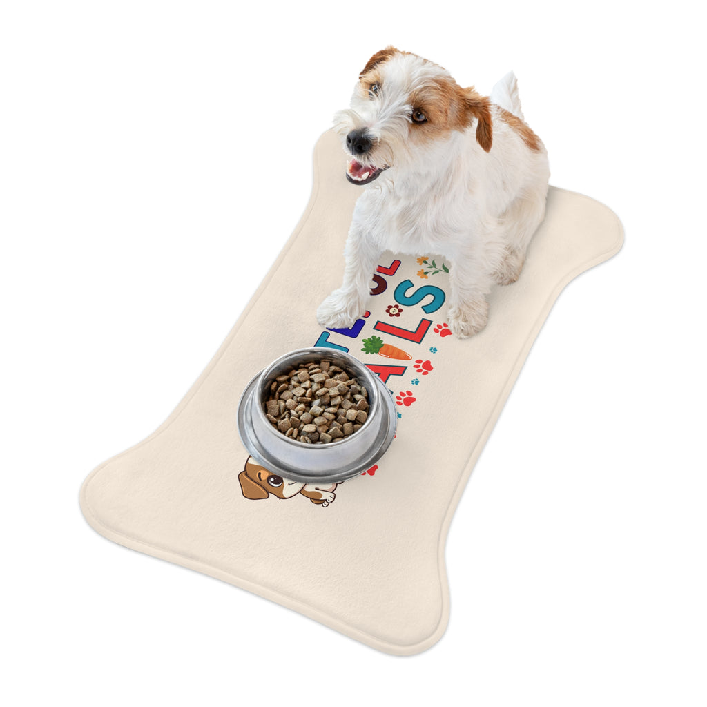 Small white and brown dog sitting on cream “Grateful Tails” bone-shaped pet feeding mat with metal food bowl.