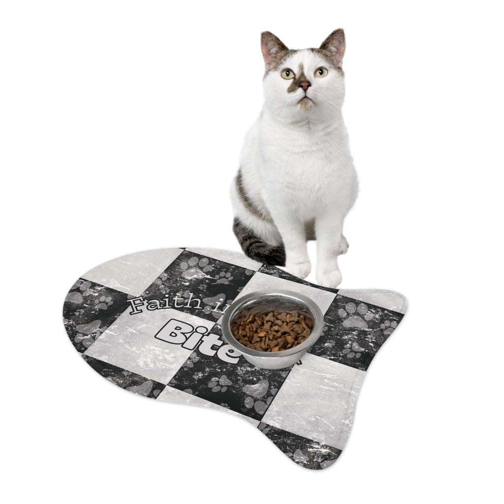 Fish‑shaped plush pet feeding mat in black and white checkerboard paw print design, featuring the phrase “Faith in Every Bite” with a cat and a cat bowl on top of it.
