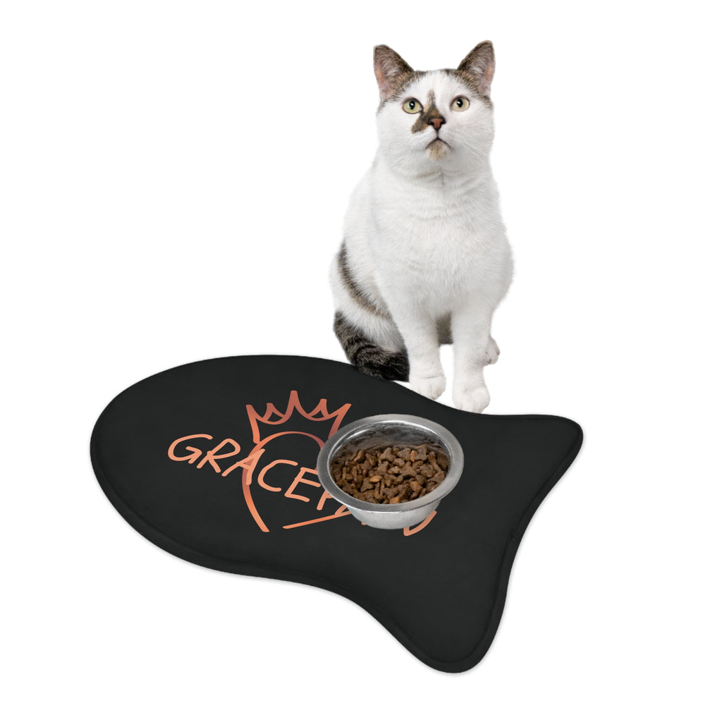 Black fish-shaped pet feeding mat with a heart and crown graphic and the word “GRACEPAW” in peach lettering, designed for comfort and non-slip functionality. A cat is n front of a feeding pet bowl on top of the mat.