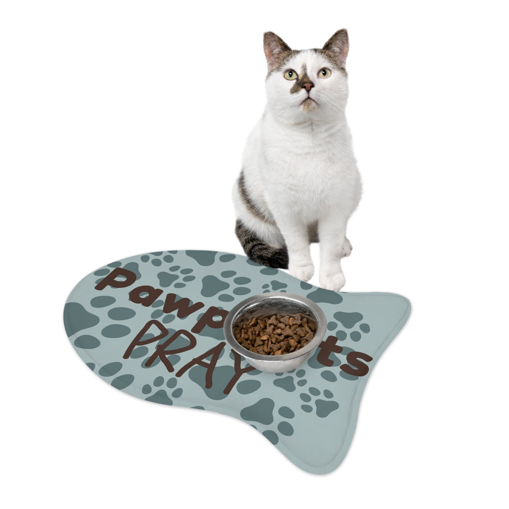 Fish‑shaped plush pet feeding mat with aqua background, dark grey paw print pattern, and brown text “Pawprints Pray”.