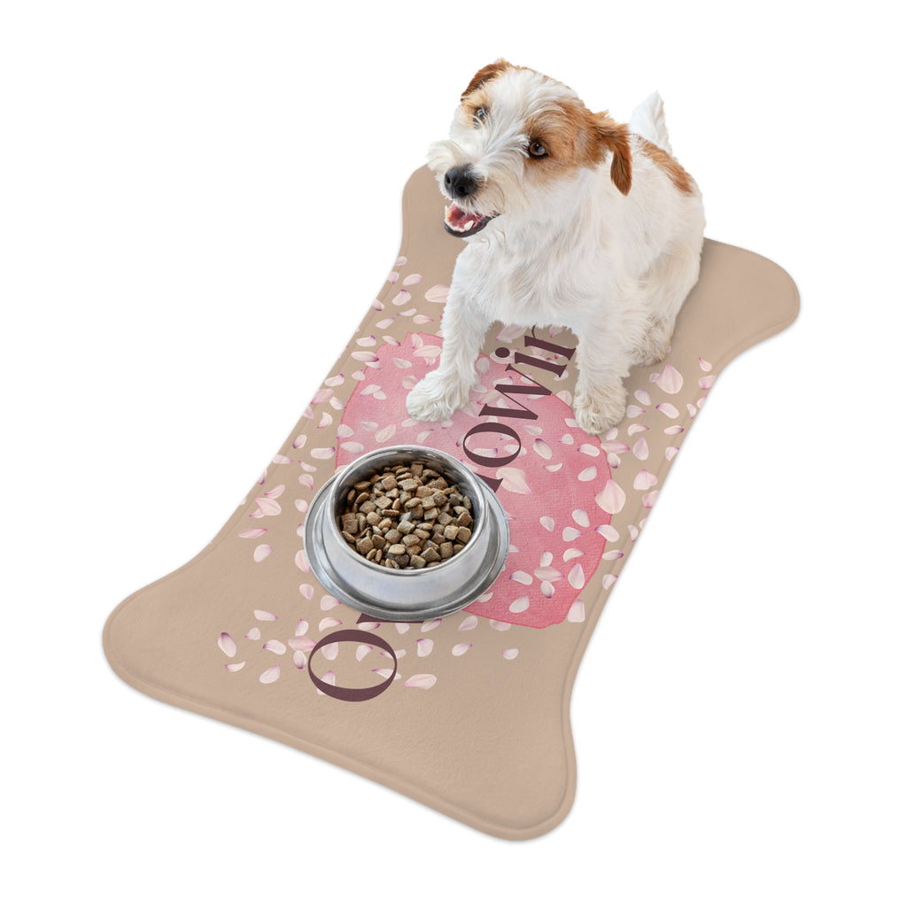 Beige pet feeding mat with pink petal design and the word “Overflowing” printed across the center placed in a room. Ad dog is standing on top of the mat with a dog bowl.
