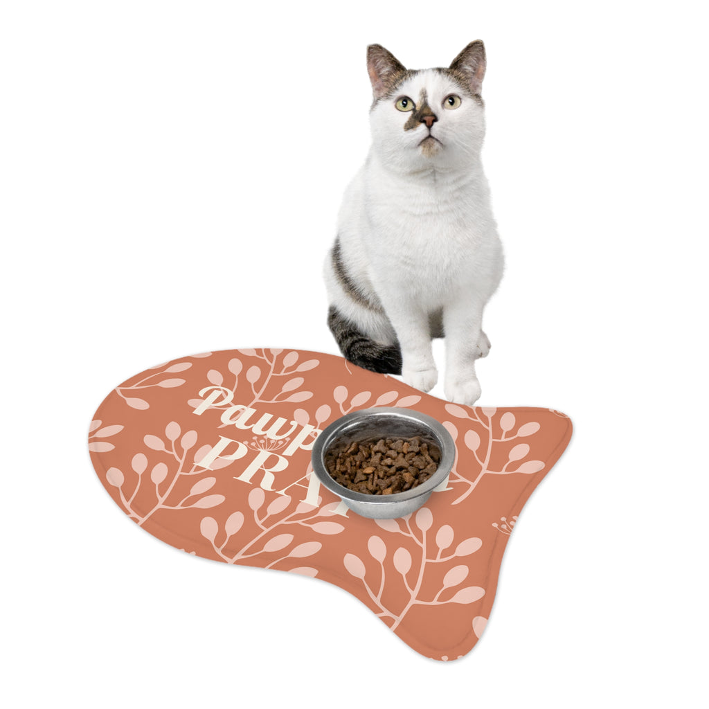 White cat with brown markings sitting next to fish-shaped feeding mat with autumn floral pattern.