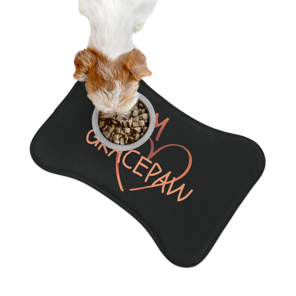 Black bone-shaped pet feeding mat with a heart and crown graphic and the word “GRACEPAW” in peach lettering, designed for comfort and non-slip functionality. There is a dog eating from a pet bowl on top of the mat.