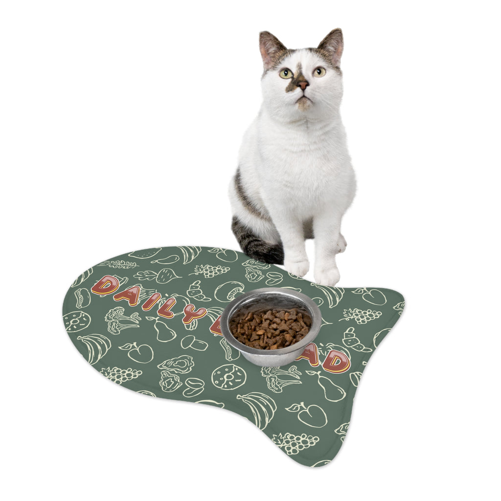 White and gray cat sitting beside fish-shaped sage green feeding mat with white doodle pattern and food bowl.