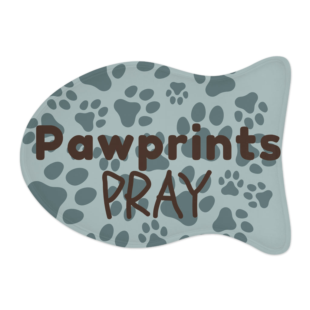 Fish‑shaped plush pet feeding mat with aqua background, dark grey paw print pattern, and brown text “Pawprints Pray”.