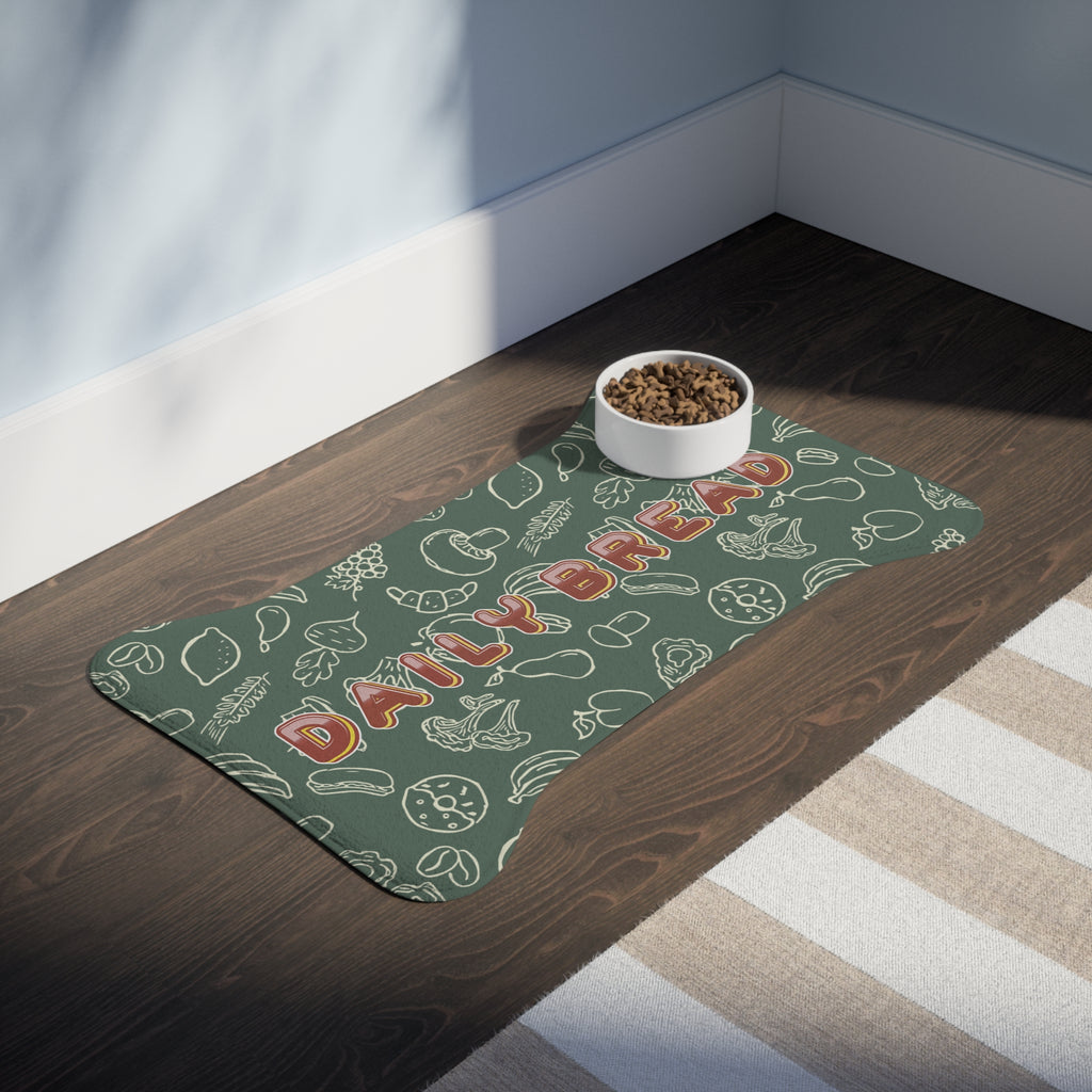 Sage green bone-shaped pet feeding mat with white doodle pattern placed on dark wood floor beside a white food bowl.