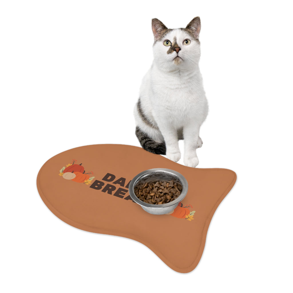 White and gray cat sitting beside a white food bowl on a fall-themed pet feeding mat with pumpkin and leaf print