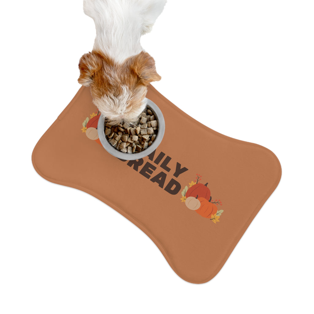 Brown and white dog sitting beside a white food bowl on a fall-themed pet feeding mat with pumpkin and leaf print
