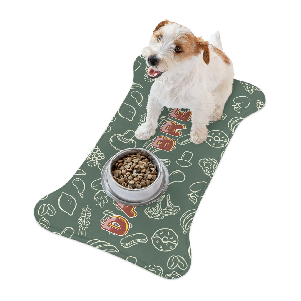 Small dog standing next to a bowl placed on sage greenl pet feeding mat with white doodle pattern.