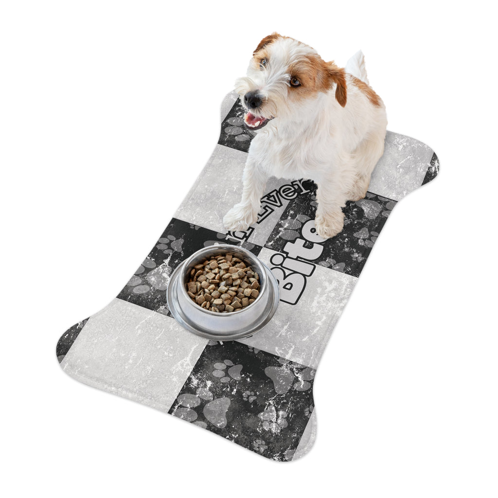 Bone‑shaped plush pet feeding mat in black and white checkerboard paw print design, featuring the phrase “Faith in Every Bite” with a dog and the dog bowl on top of mat.