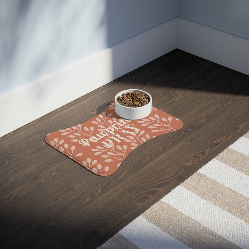 Terracotta bone-shaped pet feeding mat with white floral print and food bowl on dark wood floor near striped rug.