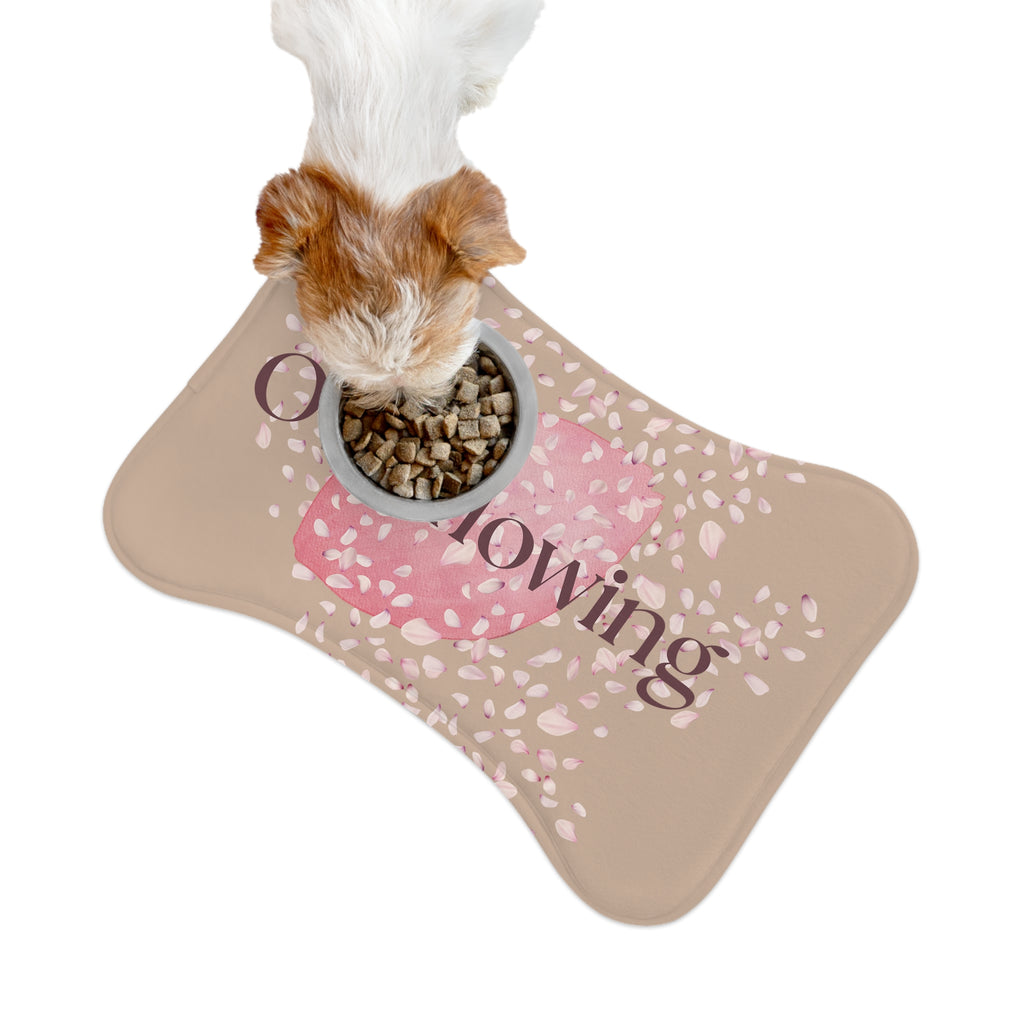 Beige pet feeding mat with pink petal design and the word “Overflowing” printed across the center – symbolizing faith, love, and abundance at mealtime. A dog is shown eating from a dog bowl on top of the mat.