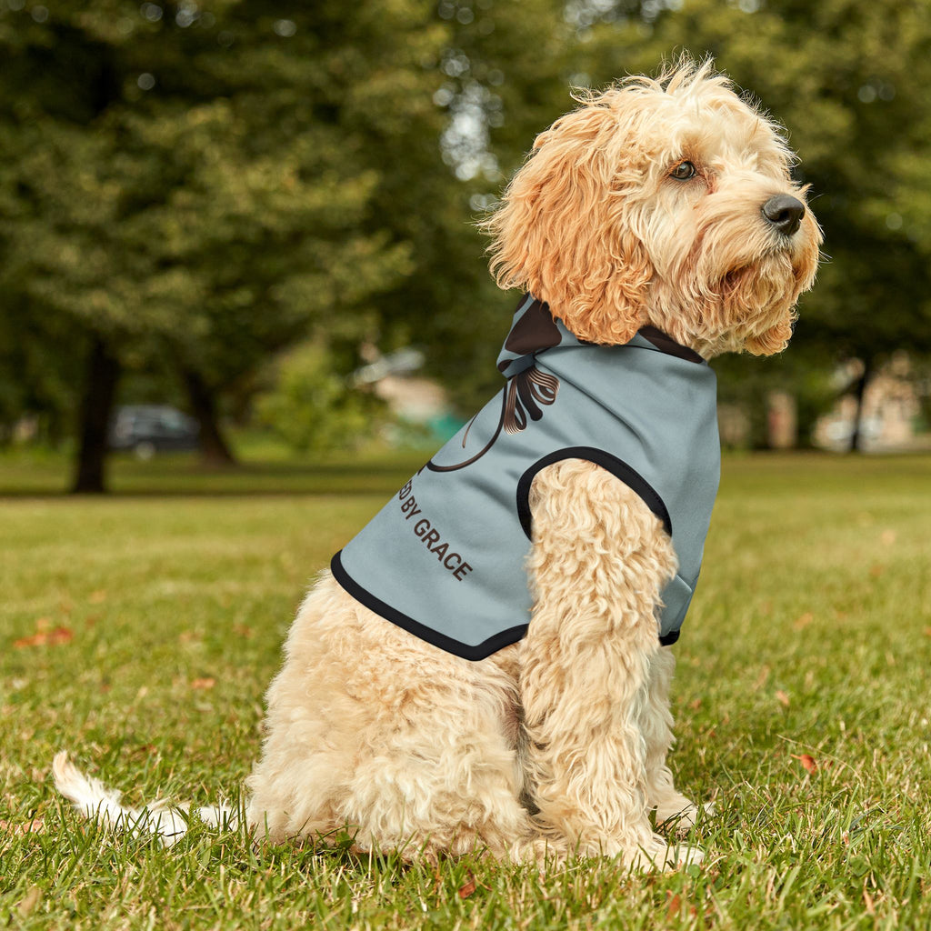 Fluffy light tan dog in a park wearing the blue gray hoodie, looking up, showing the dark brown paw print pattern on the hoodie and black trim. 