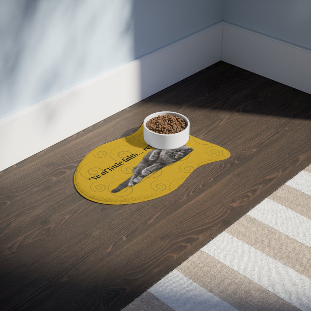 Faith-inspired cat feeding mat on dark wood floor with food bowl, featuring gray cat graphic and playful quote.