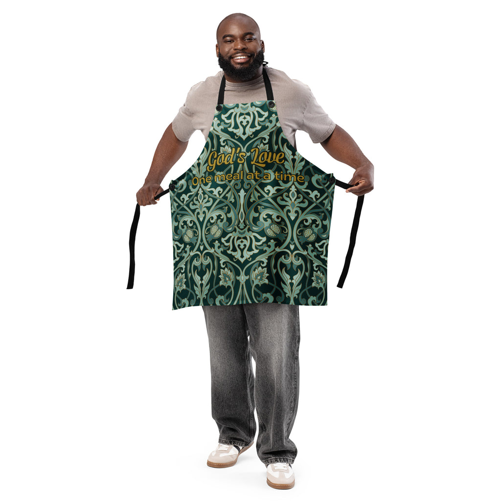 Faith-inspired apron with ornate sage and emerald baroque-style floral pattern, featuring the phrase “God’s Love  One Meal at a Time” in elegant gold lettering across the chest.