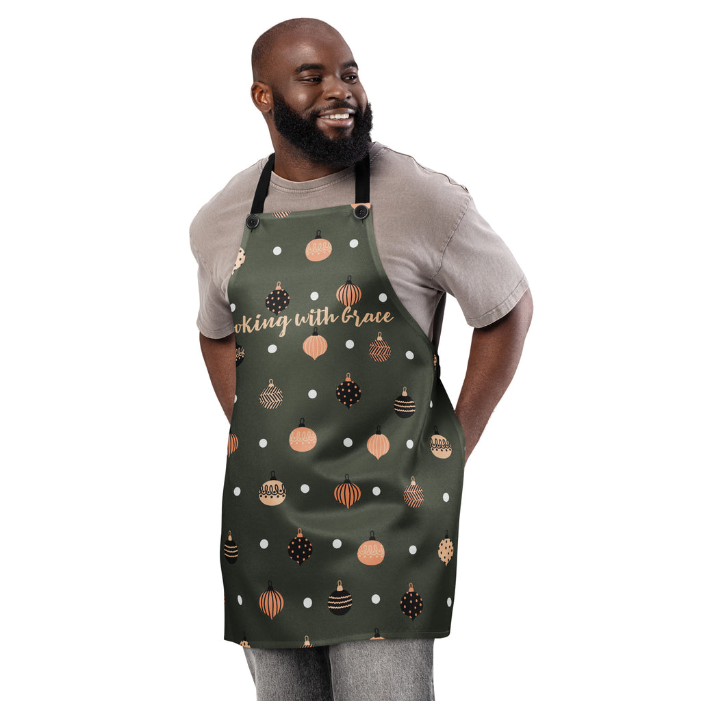 Man wearing apron, designed with Christmas ornaments with the phrase, " Cooking with Grace".