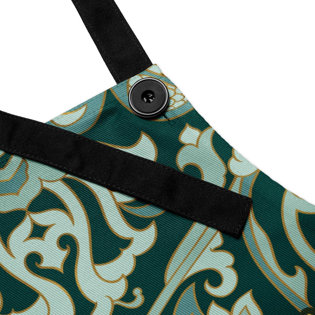 Faith-inspired apron with ornate sage and emerald baroque-style floral pattern, featuring the phrase “God’s Love  One Meal at a Time” in elegant gold lettering across the chest.