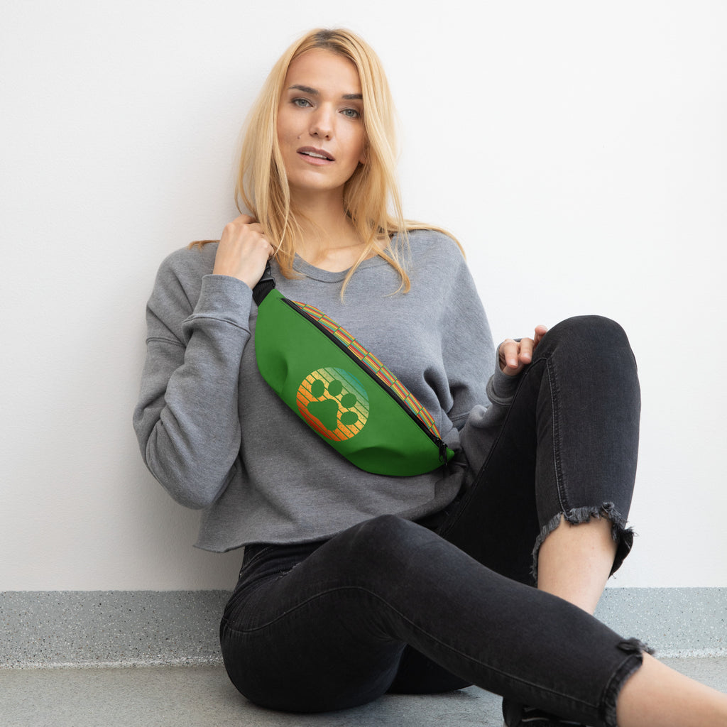 Model wearing green Paw & Praise Fanny Pack with paw print emblem across the chest, paired with casual grey sweatshirt and black jeans.