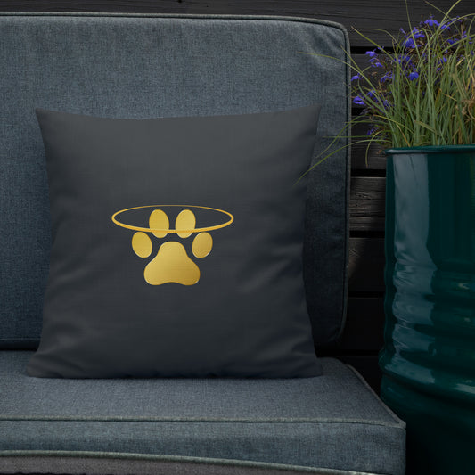 Dark grey pillow with a gold paw print design on a denim couch next to a potted plant.