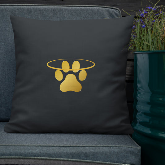 Dark grey pillow with gold paw print design on a denim couch next to a potted plant.