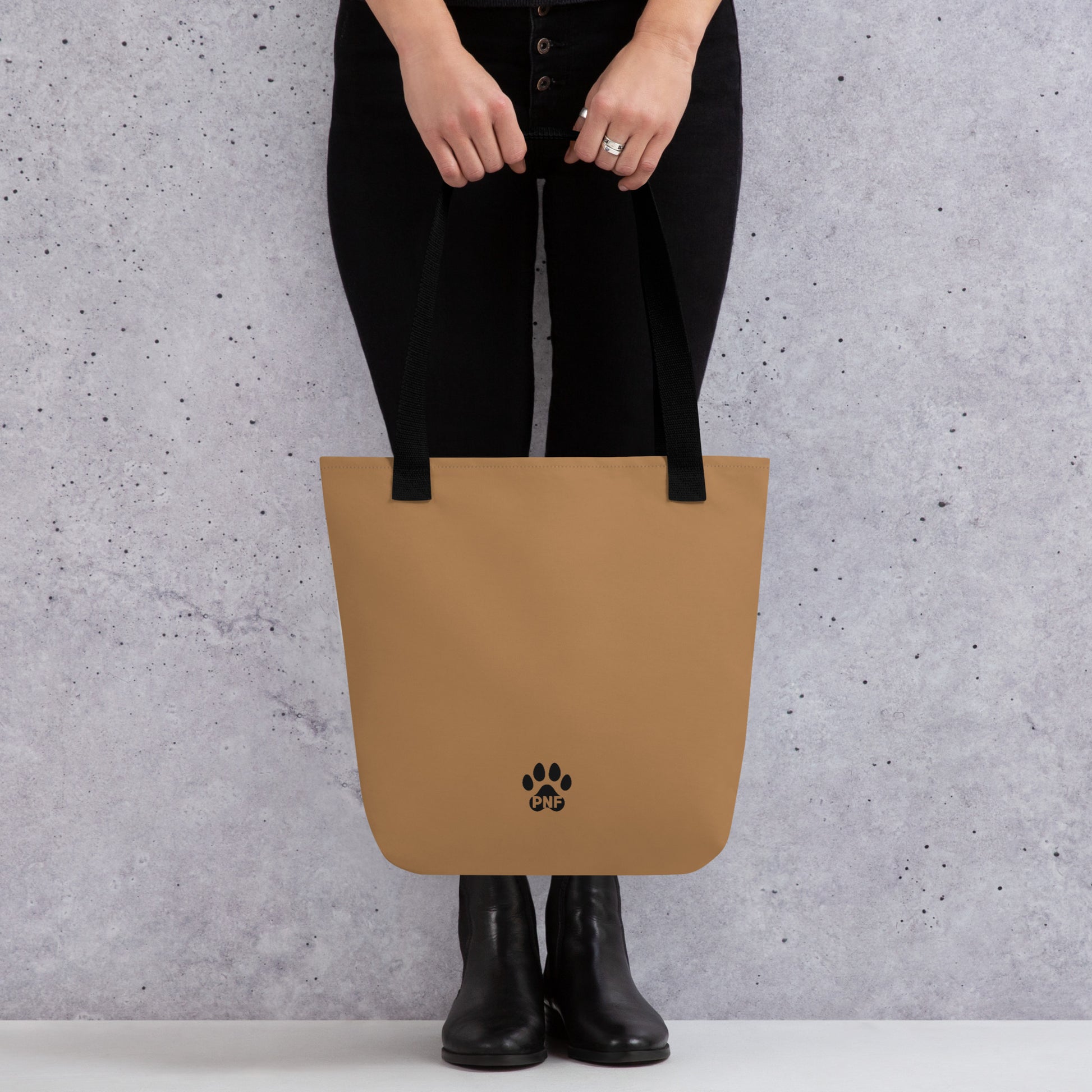 Person holding a tan tote bag with a paw print logo against a gray background