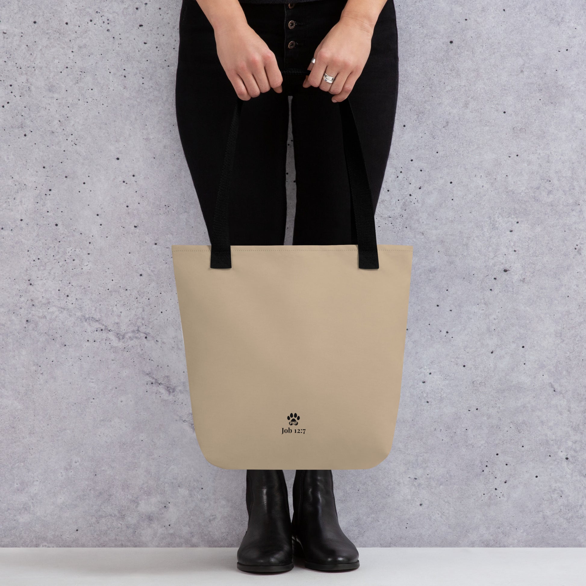 Person holding a beige tote bag with a brand logo against a gray background