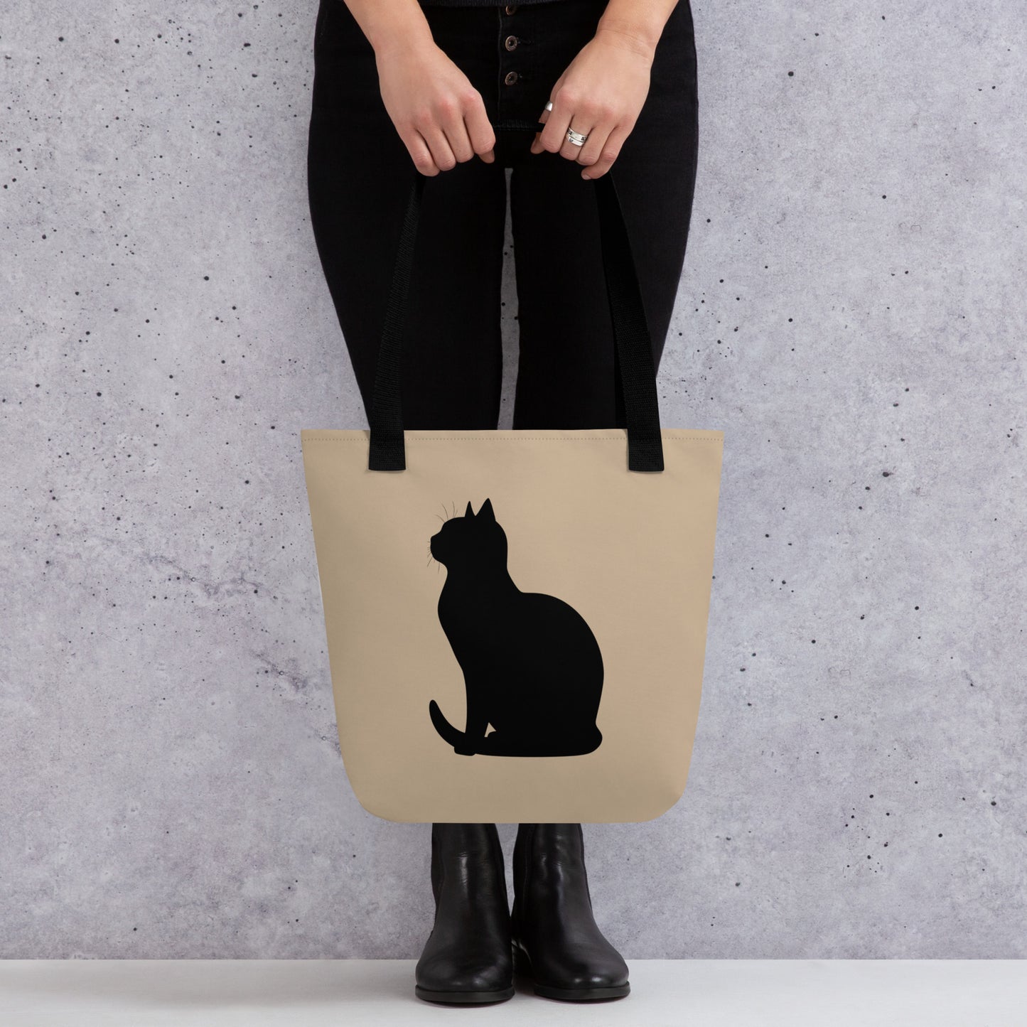 Person holding a beige tote bag with a black cat silhouette against a gray background