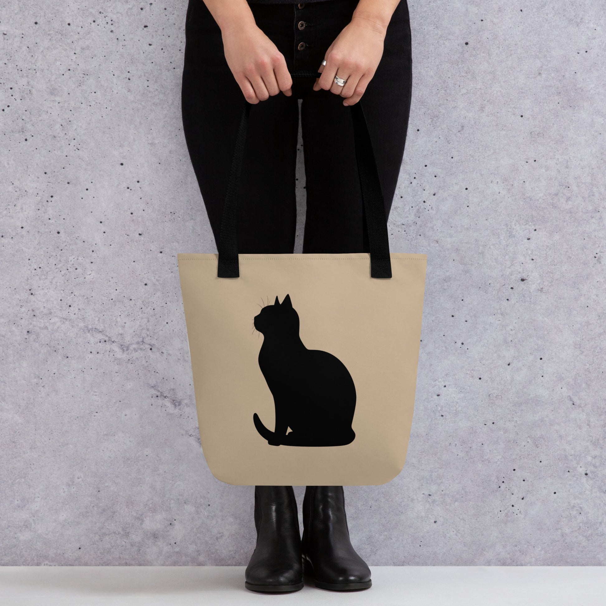 Person holding a beige tote bag with a black cat silhouette against a gray background