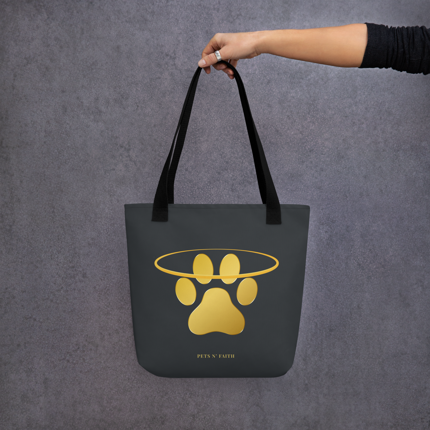Dark Gray tote bag with gold paw print design held by a hand against a gray background