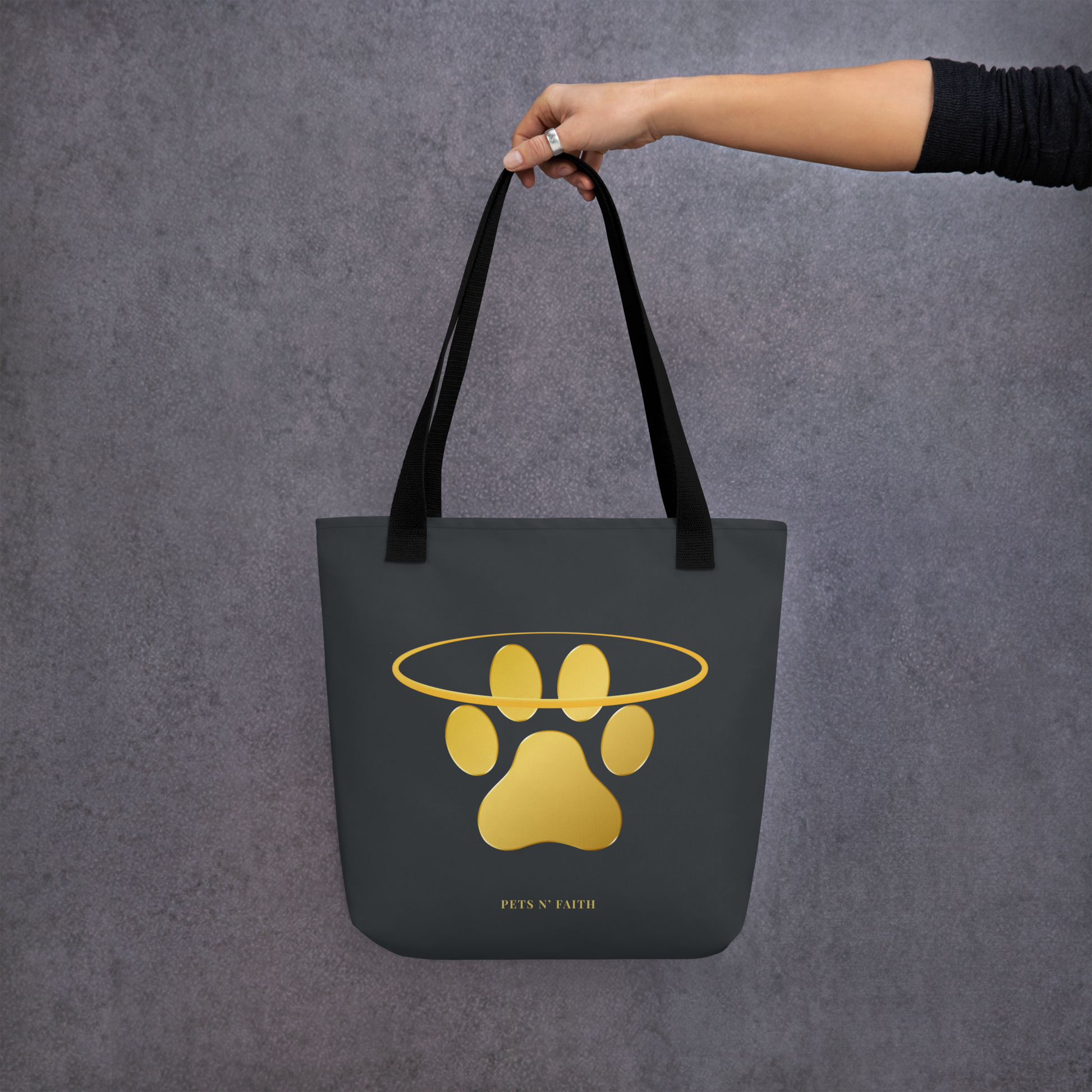 Dark Gray tote bag with gold paw print design held by a hand against a gray background