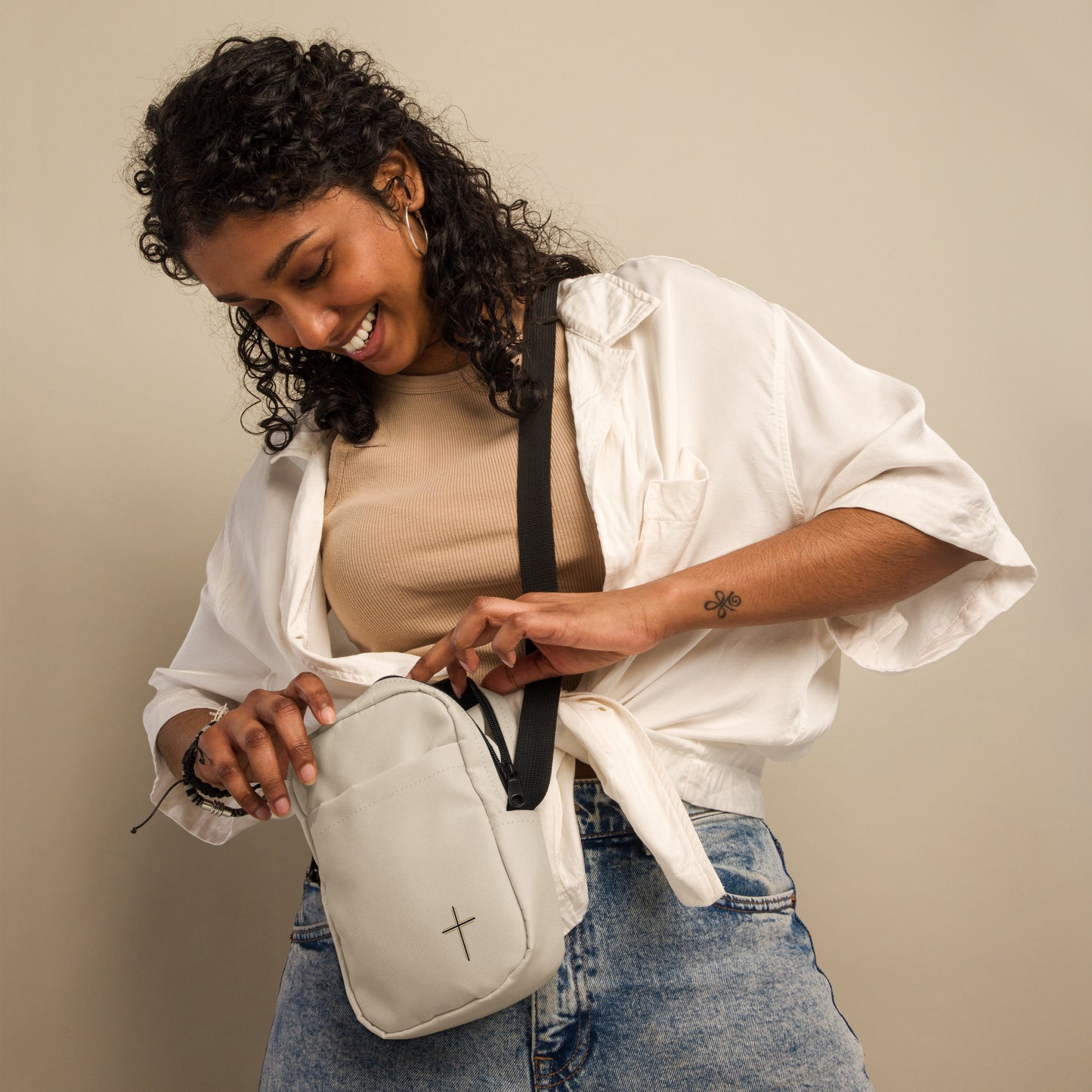 Woman holding a light gray crossbody bag against a beige background