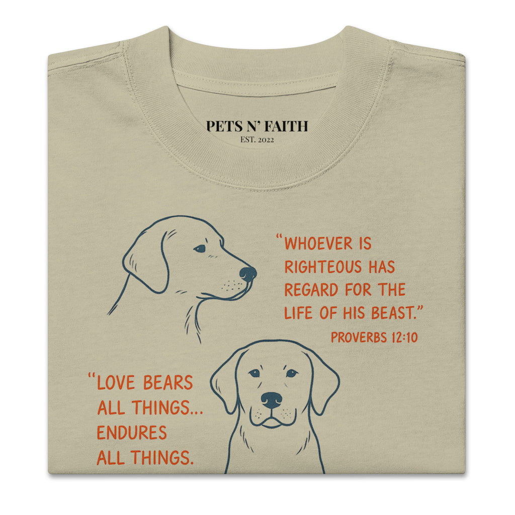 Folded tan oversized faded t-shirt with dog illustrations and Bible verses, including Proverbs 12:10, 1 Corinthians 13:7, and Matthew 10:29, designed by Pets N Faith.