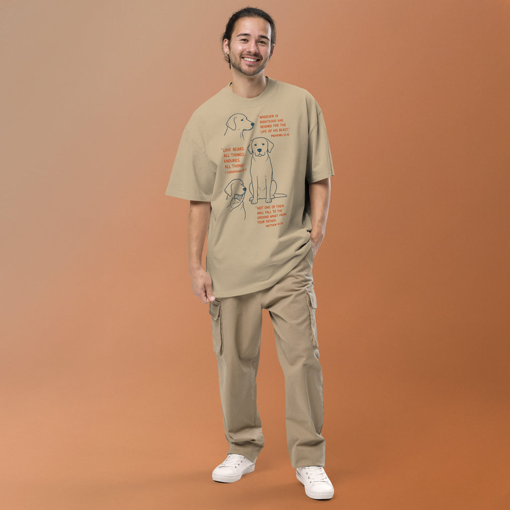 Man with khaki oversized faded t-shirt with dog illustrations and Bible verses, including Proverbs 12:10, 1 Corinthians 13:7, and Matthew 10:29, designed by Pets N Faith.