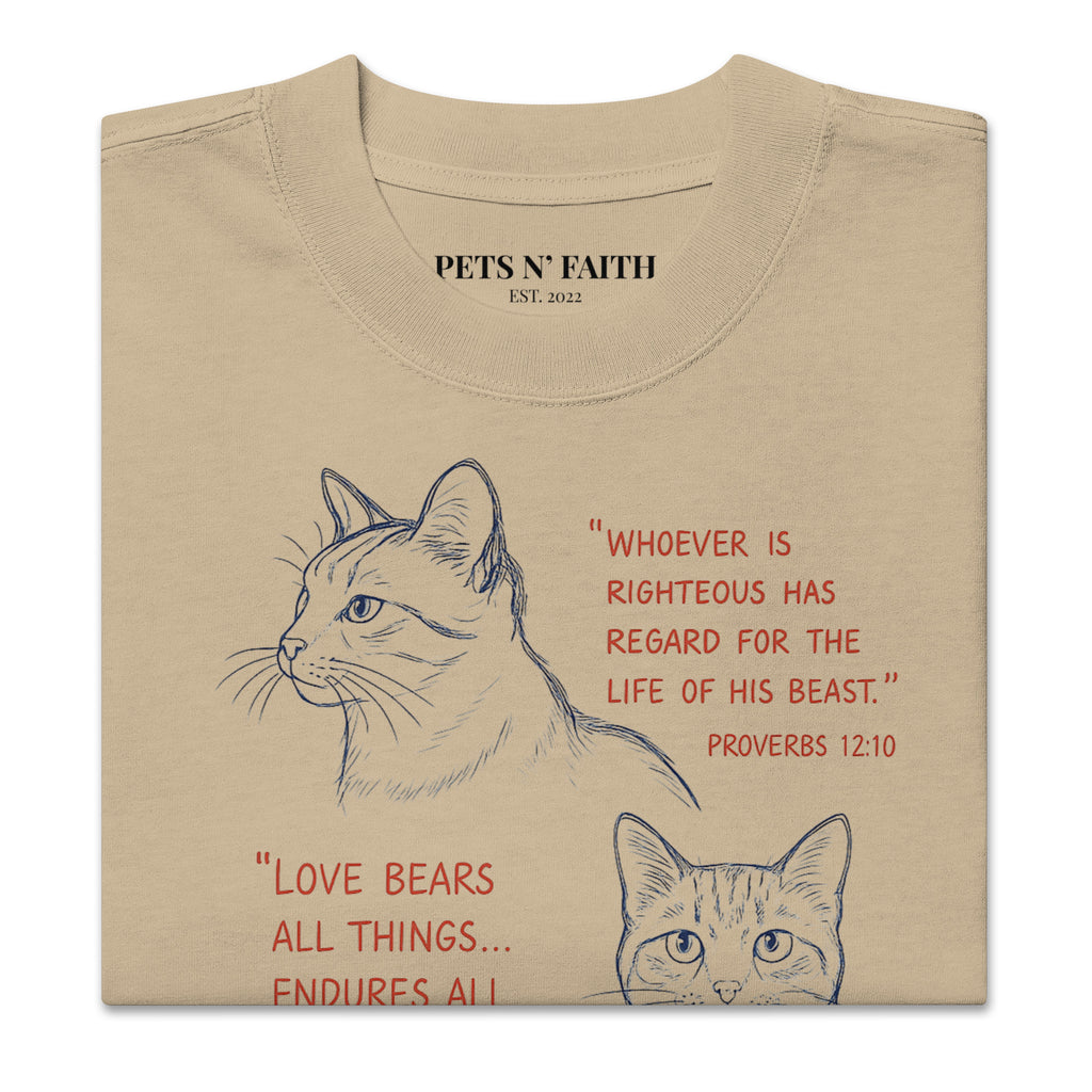 Folded view of khaki oversized faded t-shirt with cat illustrations and Bible verses, including Proverbs 12:10, 1 Corinthians 13:7, and Matthew 10:29, designed by Pets N Faith.