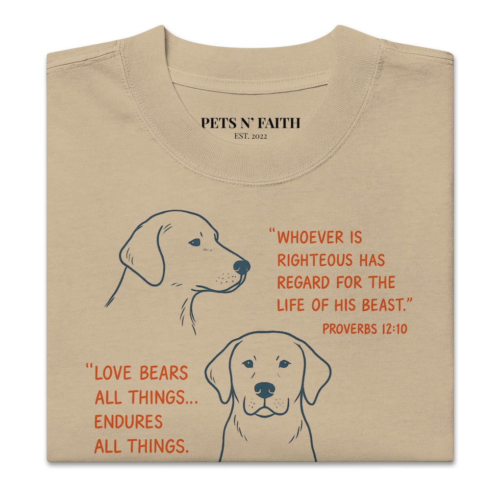 Folded khaki oversized faded t-shirt with dog illustrations and Bible verses, including Proverbs 12:10, 1 Corinthians 13:7, and Matthew 10:29, designed by Pets N Faith.