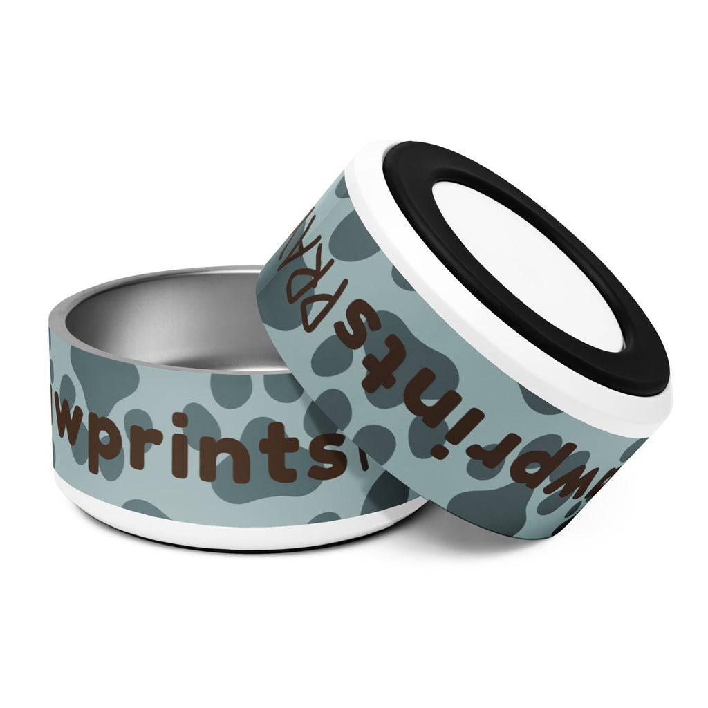 Stainless steel pet bowl with soft blue background and scattered dark paw prints, featuring the text “Pawprints Pray” in brown bold and handwritten font.