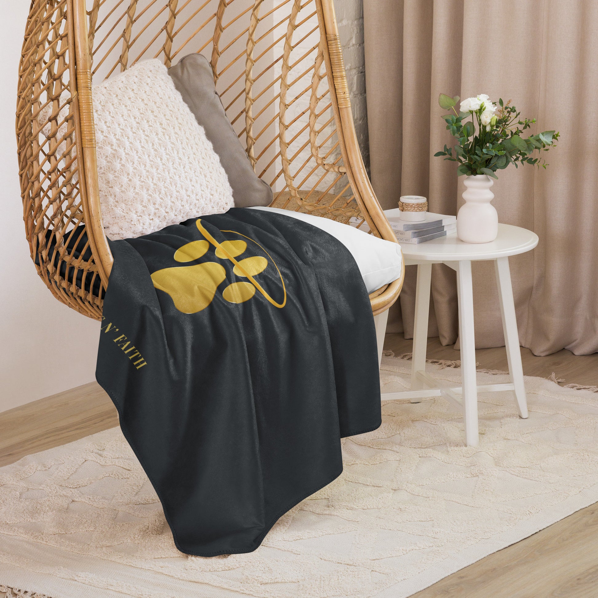 Black blanket with a gold logo draped over a wicker chair in a cozy room.