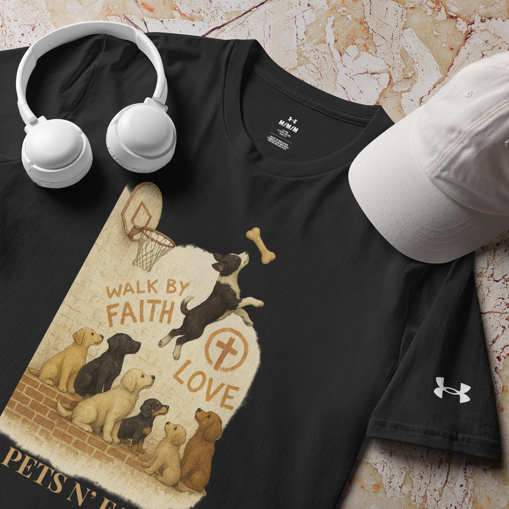 Close-up of black Under Armour Pets N’ Faith Performance T-Shirt with “ Walk by Faith and Love” design, next to a white hat and white headphones. The Pets N' Faith logo is in gold text.