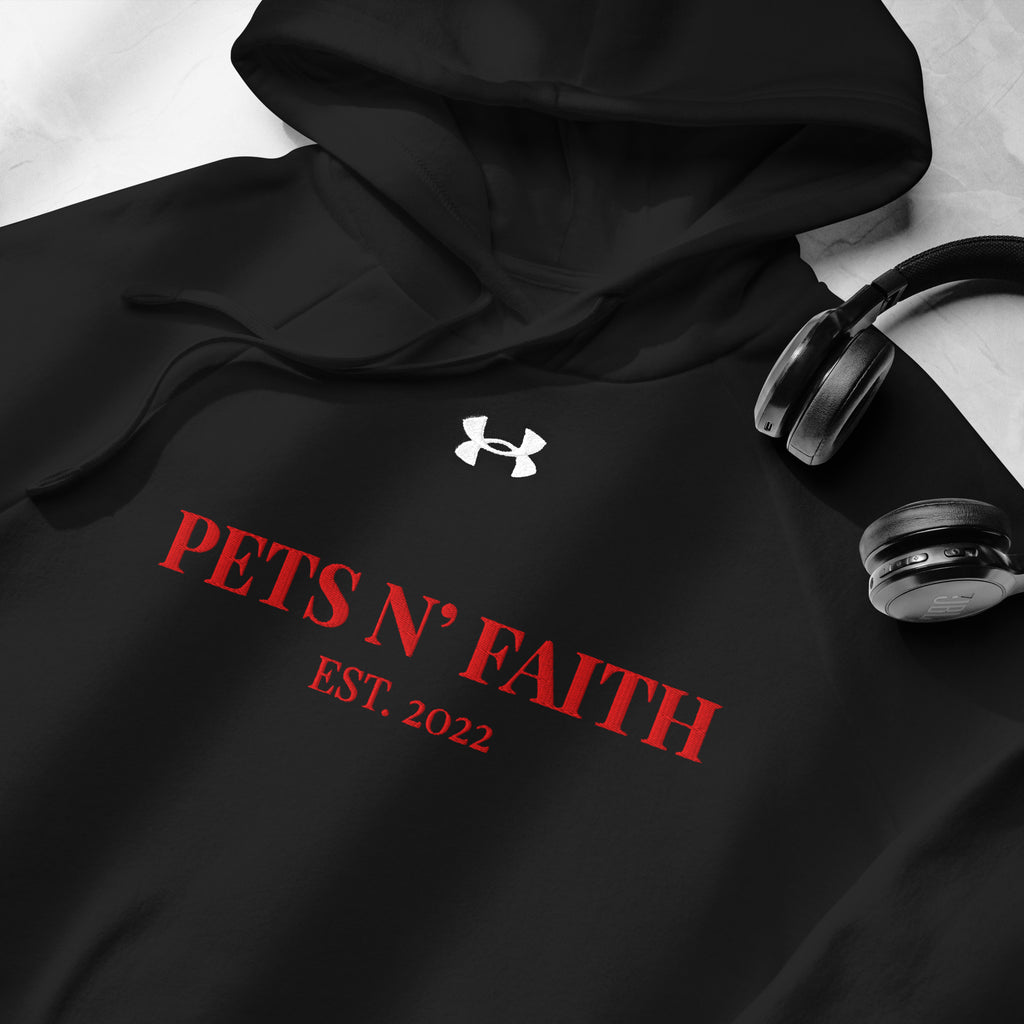 Close-up of black Under Armour Pets N’ Faith Hoodie with red print and drawstring hood, next to wireless headphones