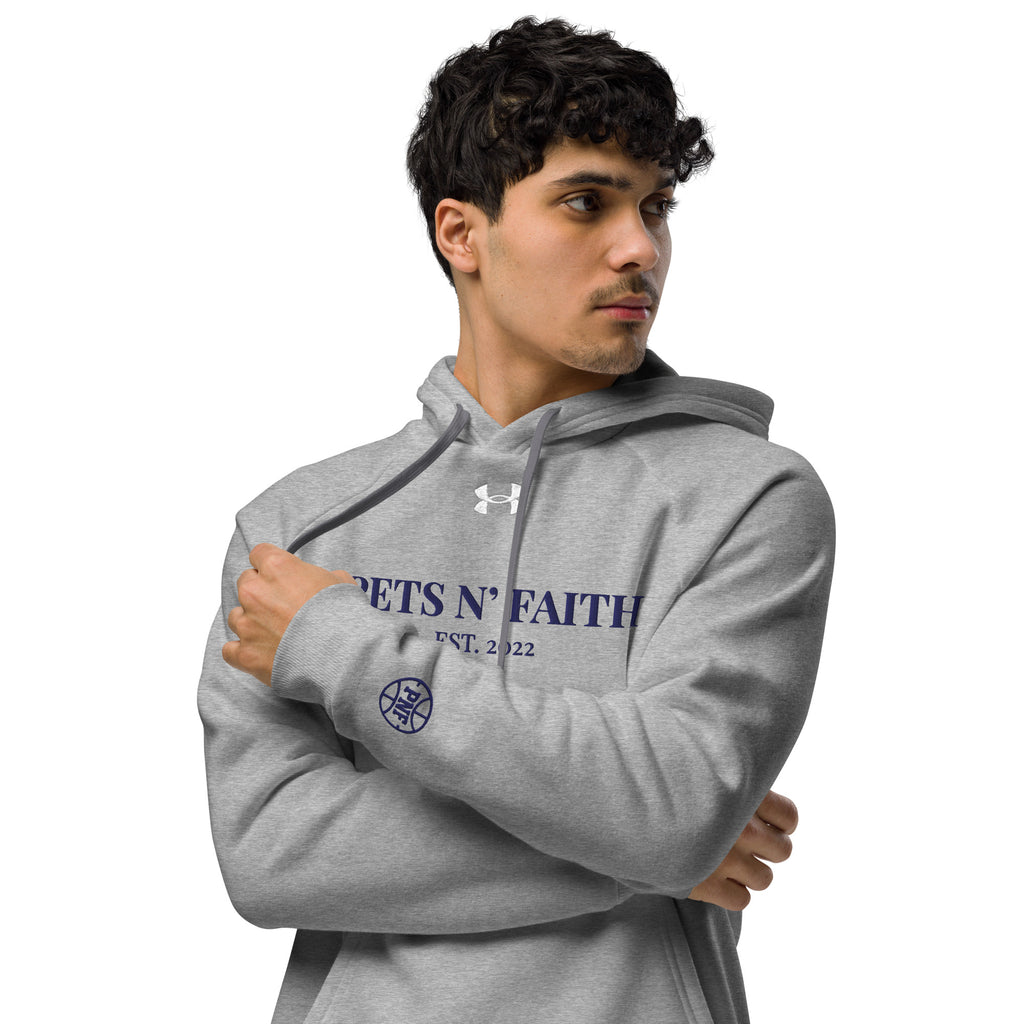 Man wearing light gray Under Armour Pets N’ Faith Hoodie with gold text and sleeve emblem