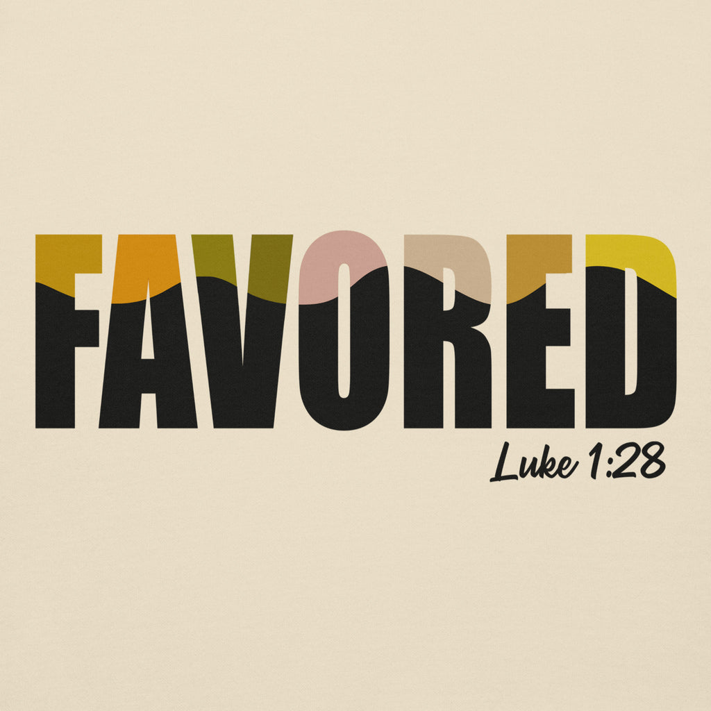Close-up of multicolor “Favored” text with Luke 1:28 Bible verse on cream-colored Unisex hoodie fabric